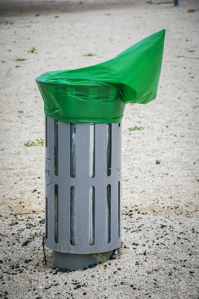 Green plastic bag stretched over a gray trash bin